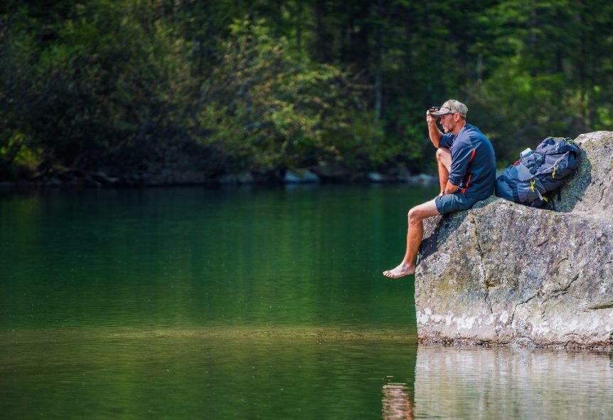 man sitting on rock by lake
